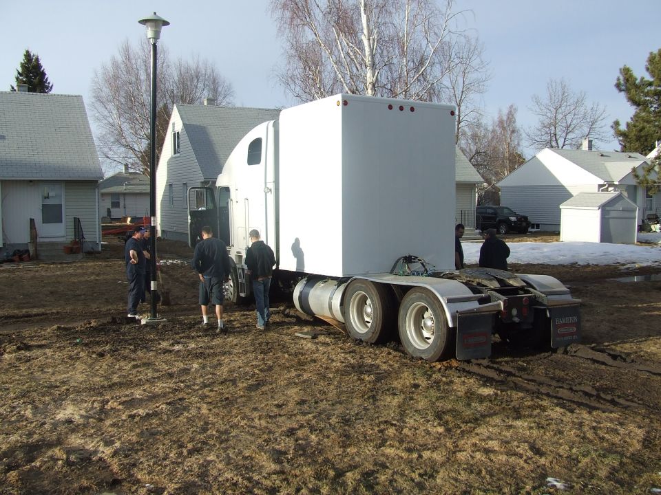 White semi-trailer truck with a box trailer, viewed from the rear, parked on muddy ground