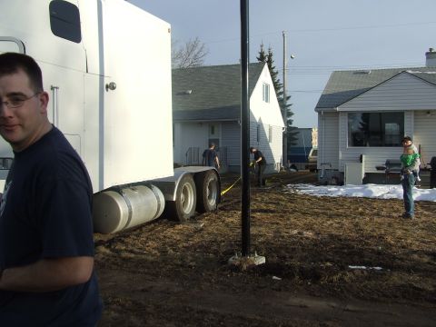 1990 Ford Bronco - A man stands near the trailer of a semi-truck while others work in a muddy yard with houses visible.