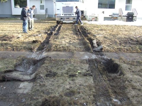 1990 Ford Bronco - A white truck is stuck in the mud, leaving deep tracks in the yard. People stand nearby observing the situation.