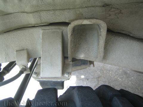 1987 Suzuki Samurai - Underside view of a vehicle's frame showing a suspension component and a large tire tread.