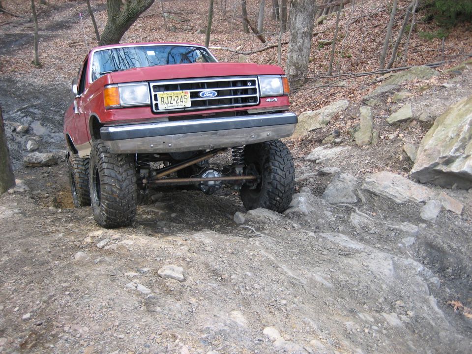 1990 Ford Bronco navigating a steep, rocky trail with lifted suspension and large tires
