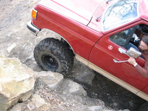 1990 Ford Bronco - A red Ford truck maneuvers over rocks on an off-road trail.