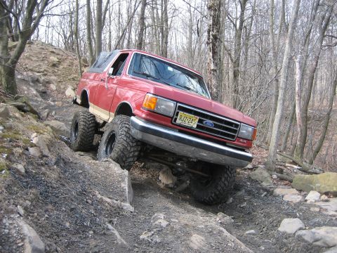 1990 Ford Bronco - This red 1990 Ford Bronco is shown tackling a challenging off-road trail with steep inclines and large rocks.