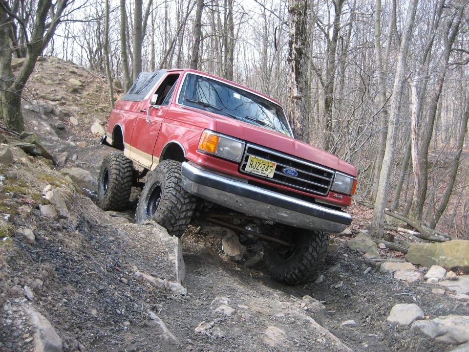 Red 1990 Ford Bronco navigating rocky terrain