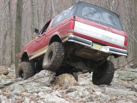 1990 Ford Bronco - A red 1990 Ford Bronco navigates a rocky trail with its suspension flexed.