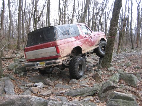 1990 Ford Bronco - This red 1990 Ford Bronco navigates a rocky trail, demonstrating its off-road capabilities.