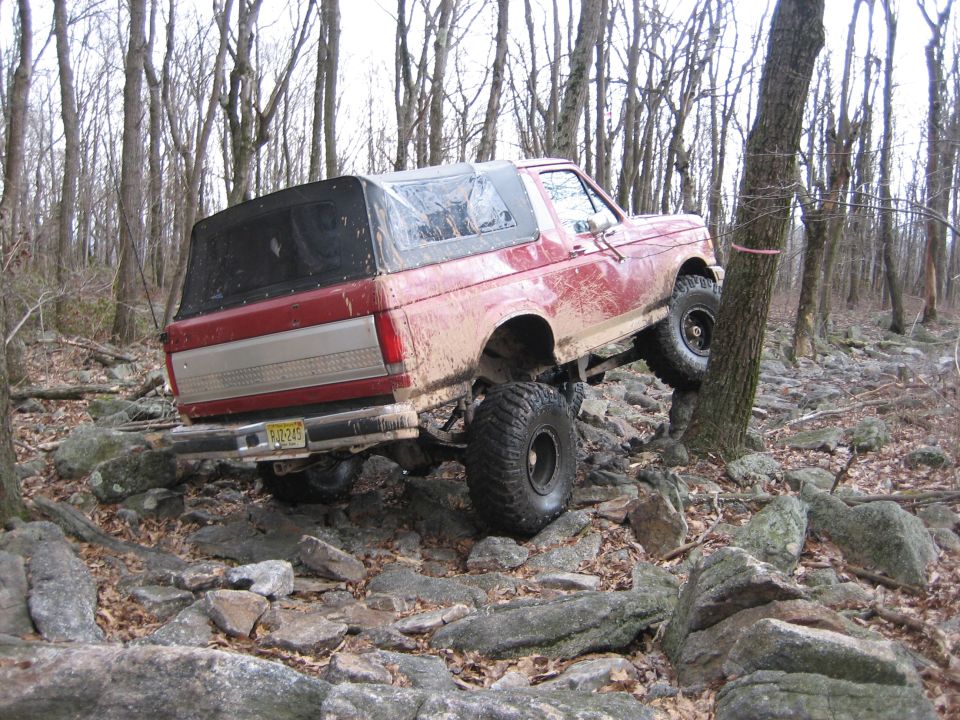 Red 1990 Ford Bronco climbing rocks, rear 3/4 view