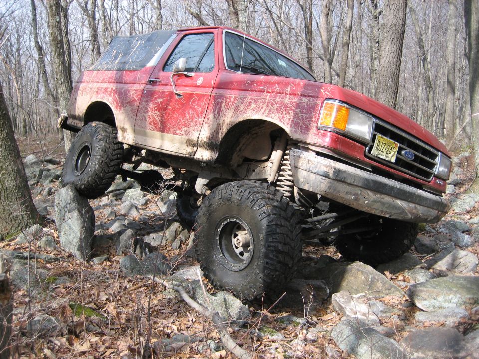 1990 Ford Bronco with lifted suspension and large tires navigating rocky terrain
