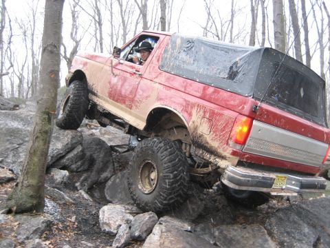 1990 Ford Bronco - This red Ford Bronco is navigating a difficult rocky terrain, with one wheel lifted high off the ground.