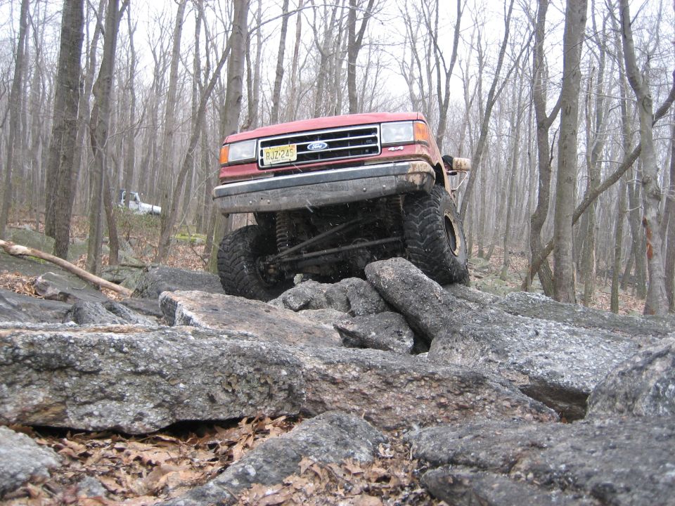 Red Ford Bronco climbing over rocks, front end lifted high