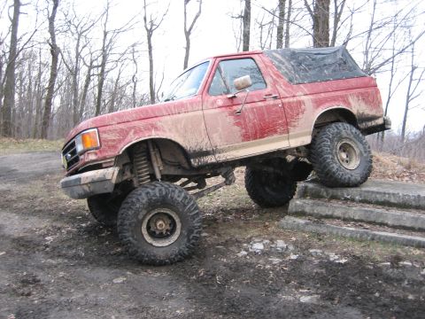 1990 Ford Bronco - This lifted 1990 Ford Bronco navigates an obstacle course, its red paint covered in mud.