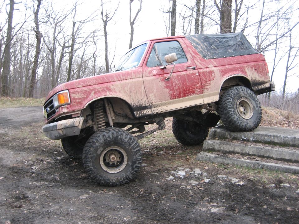 Red 1990 Ford Bronco climbing concrete steps, lifted with off-road tires