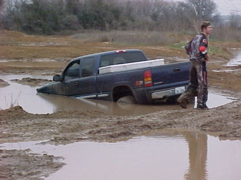1978 Ford Bronco - A person stands by as a pickup truck is submerged in a muddy area.