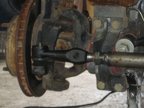1990 Ford Bronco - Steering linkage component, likely a tie rod end, shown with a brake rotor in the background.
