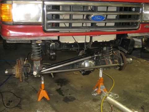 1990 Ford Bronco - Front axle and suspension of a red Ford truck, likely from the 1990s, is visible with the grille and headlights.