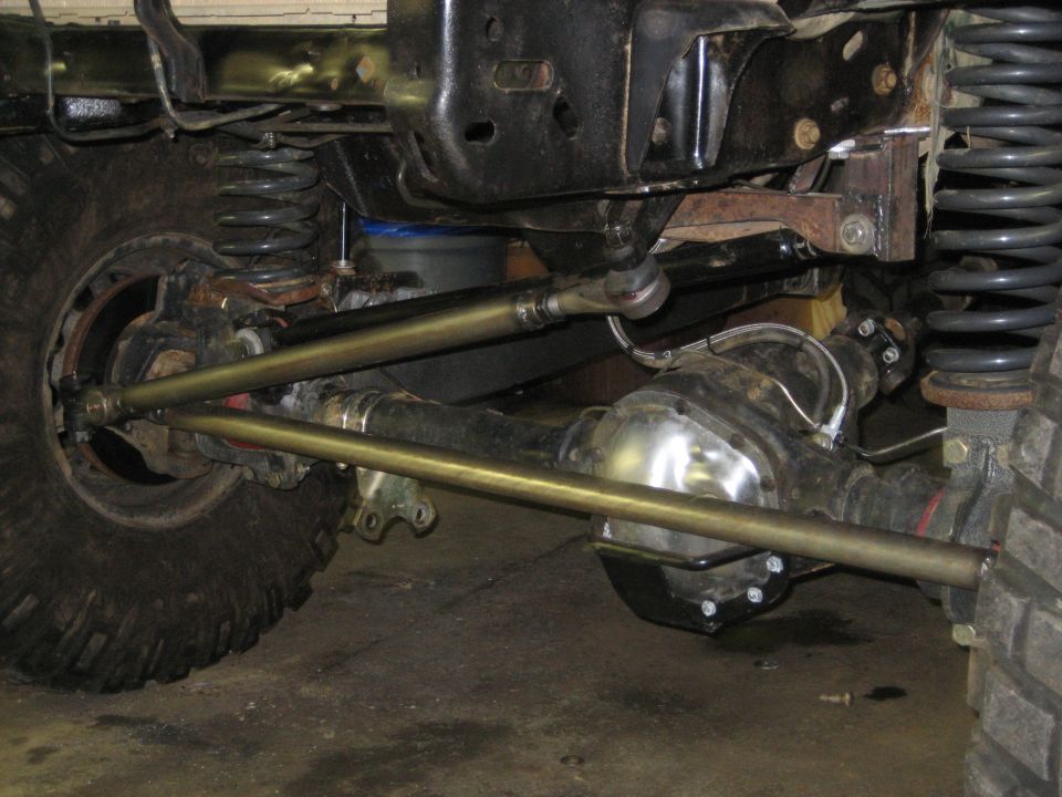 Close-up of a vehicle's front axle, steering linkage, and suspension with large tires