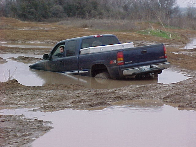 Dark blue pickup truck stuck in mud, side view. Silver toolbox in bed