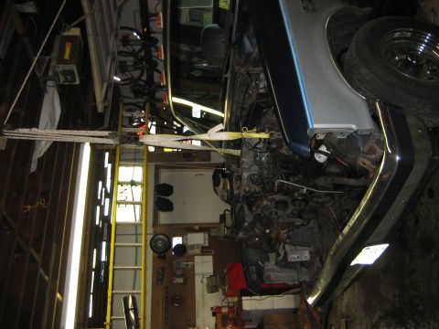 1990 Ford Bronco - The engine bay of a Ford Bronco is shown with the engine hoisted out, suspended by straps in a workshop.