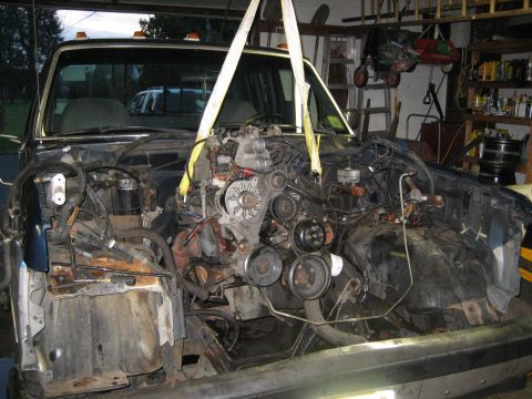 1990 Ford Bronco - The engine is being removed from the truck using a hoist, with the front end of the vehicle partially dismantled.