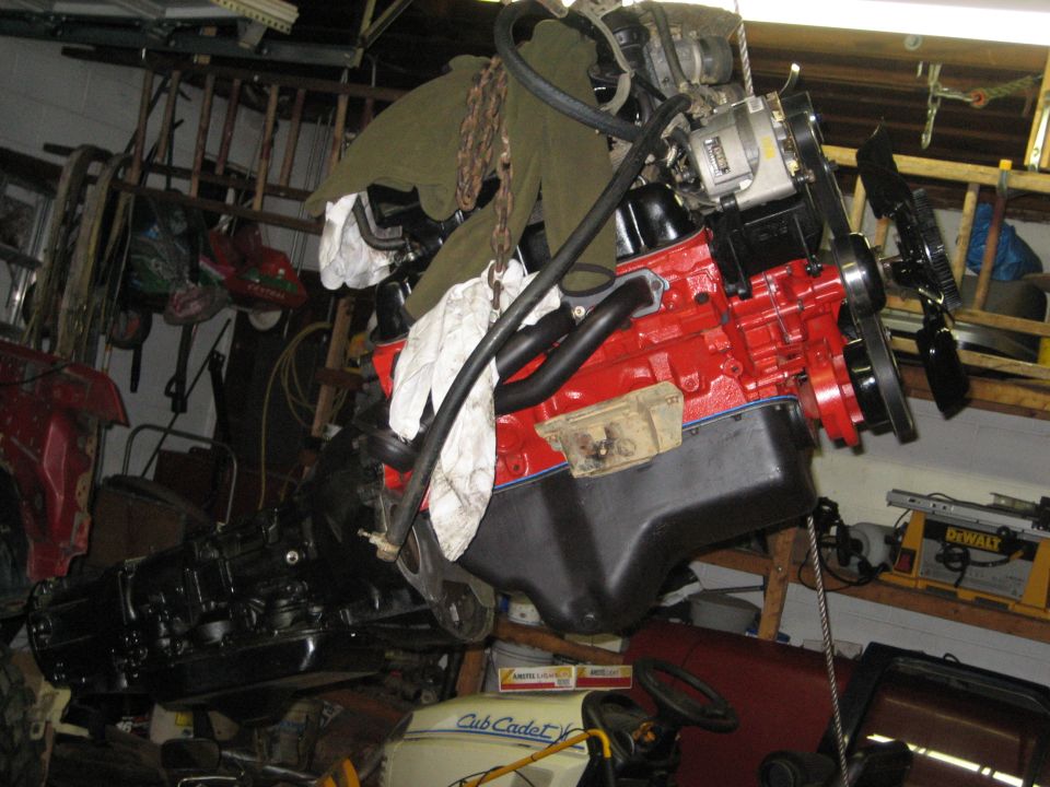 Red engine block with black oil pan and exhaust manifolds, suspended by chains