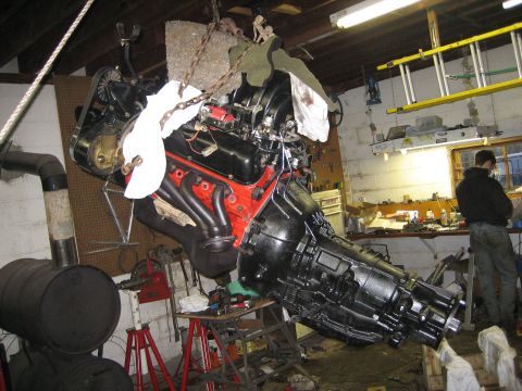 1990 Ford Bronco - Engine and transmission assembly hoisted in a workshop, with a person standing in the background.