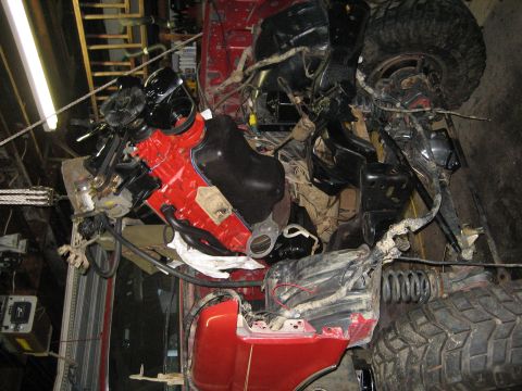 1990 Ford Bronco - Close-up view of a red vehicle's engine and suspension system, possibly undergoing repairs or modifications.
