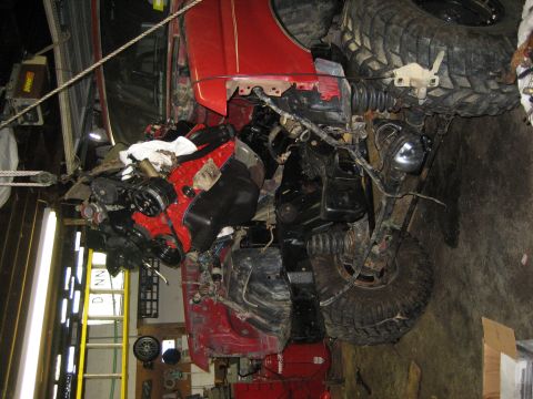 1990 Ford Bronco - The vehicle's engine is exposed and partially disassembled, with large off-road tires visible.