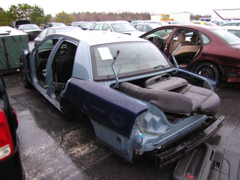 1991 Ford LTD Crown Victoria - A dismantled blue sedan sits in a junkyard, its interior exposed to the elements.