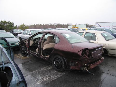 1991 Ford LTD Crown Victoria - A maroon sedan sits in a junkyard with its doors open and significant damage to the rear.