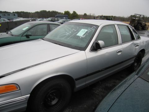 1991 Ford LTD Crown Victoria - A silver sedan sits in a junkyard with other vehicles under an overcast sky.