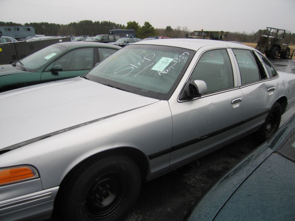 Silver sedan with black wheels and a dent on the rear passenger door. Paper on windshield says 'Strip P' and has a sticker with 'A073357'