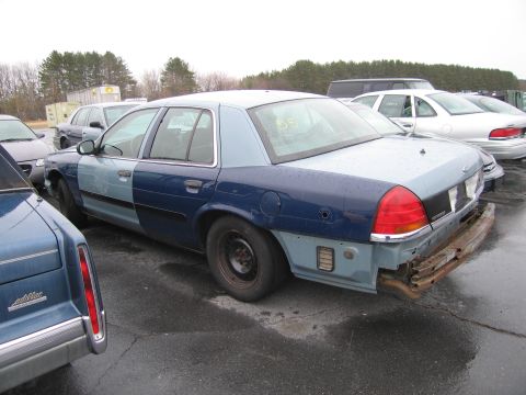 1991 Ford LTD Crown Victoria - Sedan with mismatched paint panels and a damaged rear bumper sits in a lot with other vehicles.