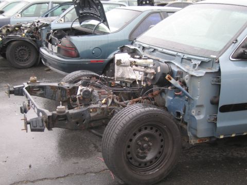 1991 Ford LTD Crown Victoria - A partially disassembled blue car sits in a junkyard, showing its chassis and engine components.