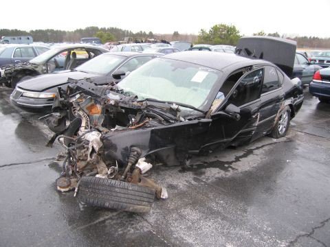 1991 Ford LTD Crown Victoria - A severely damaged black sedan sits in a junkyard with its front end completely demolished.