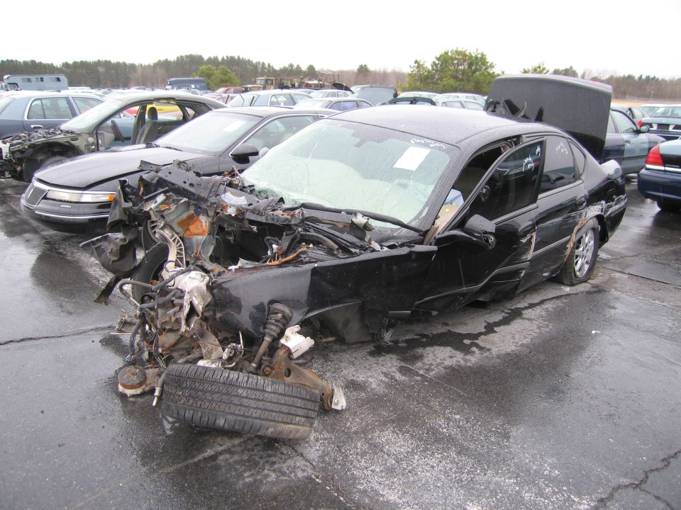 Damaged black sedan with front end destroyed, hood open, and trunk ajar
