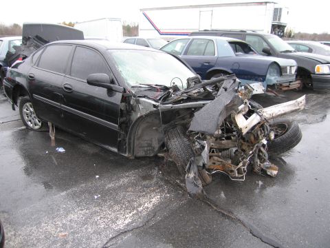 1991 Ford LTD Crown Victoria - A heavily damaged black sedan sits in a lot, its front end crushed from an apparent collision.
