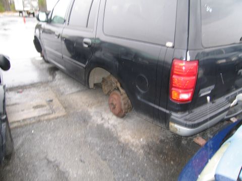 1991 Ford LTD Crown Victoria - Rear view of a black SUV with its wheels removed, sitting on a wet lot.