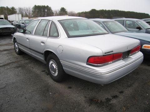 1991 Ford LTD Crown Victoria - A silver sedan is parked in a lot with other vehicles, showing its rear three-quarter profile.