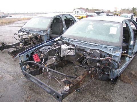 1991 Ford LTD Crown Victoria - Two sedans, stripped of their engines and body panels, sit in a lot under an overcast sky.