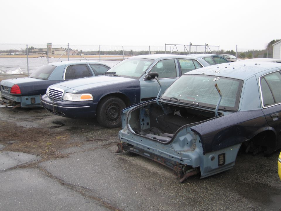 Three Ford Crown Victorias parked outside, two with rear ends missing. One has its trunk open