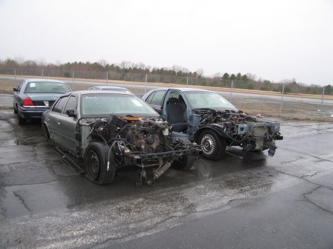 1991 Ford LTD Crown Victoria - Two 1991 Ford Crown Victoria cars sit stripped down on a wet asphalt lot.
