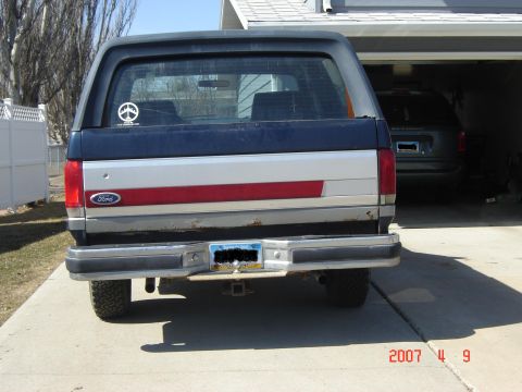 1988 Ford Bronco - Rear view of a 1988 Ford Bronco parked in a driveway, with another vehicle visible in the garage.