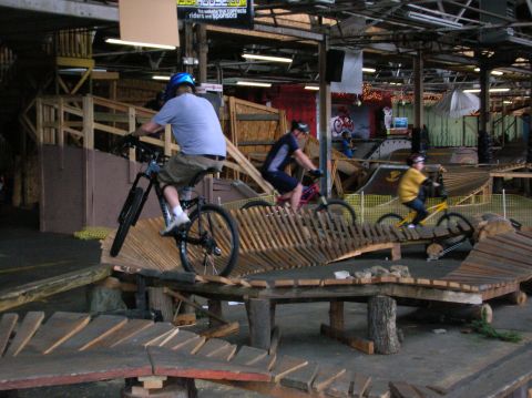 1997 Ford Probe - Several people ride mountain bikes through an indoor wooden obstacle course with ramps and jumps.