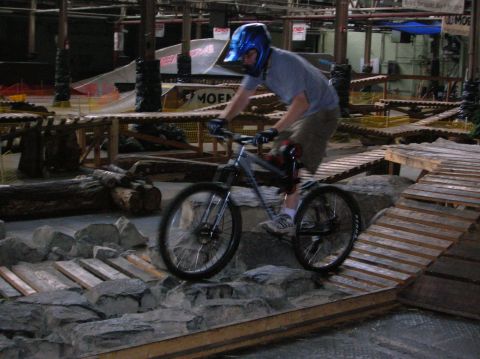 1997 Ford Probe - Mountain biker navigates a challenging indoor course with wooden ramps and obstacles.