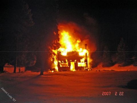 1989 Ford Bronco - A house is consumed by fire at night, with flames visible through the windows and smoke rising into the dark sky.
