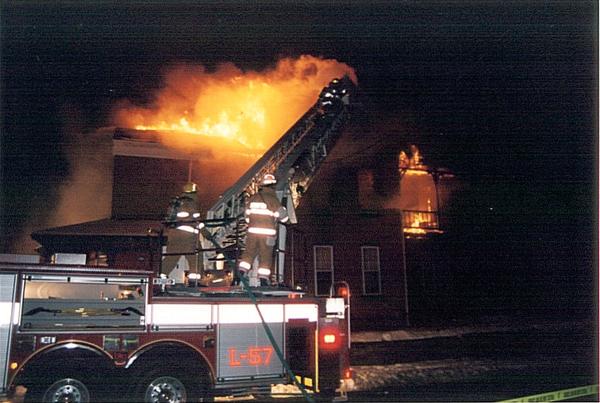 Red fire truck with ladder extended towards a burning building at night