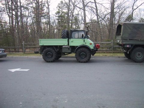 1991 Ford Bronco - A light green utility truck tows a larger military vehicle with a canvas cover.
