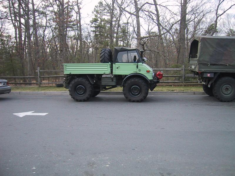 Green military truck with large tires and a spare tire on back, towing a camouflaged trailer