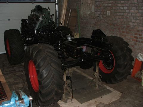 1991 Ford Bronco - The chassis of a vehicle with oversized tires and an exposed engine is shown in a garage.