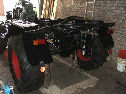 1991 Ford Bronco - The rear chassis and large tires of a tractor are visible, supported by jack stands in a workshop.